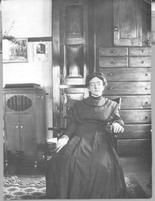 SA0063 - Alice Smith was from the Church Family. She is seated in a chair; a chest of drawers and music box are behind her. Identified on reverse., Winterthur Shaker Photograph and Post Card Collection 1851 to 1921c